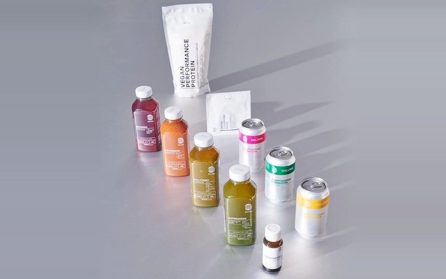 Smartphone mit dem DALUMA Health Coach Chat vor kaltgepressten Säften, Kombucha und Detox Clearing Mask.