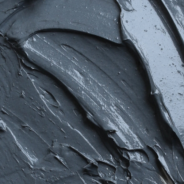 Nahaufnahme einer glatten, dunkelgrauen, cremigen Substanz mit sichtbaren Pinselstrichen und strukturierten Rillen. Die Oberfläche erscheint glänzend und in einigen Bereichen leicht reflektierend.