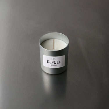 Ein silberner Nullpunkt-Kerzenhalter mit der Aufschrift DUFTKERZE GRADE 0.4 REFUEL ruht in der Draufsicht auf einer glatten grauen Fläche. Im Inneren bietet eine unbenutzte weiße Kerze einen Energie-Boost mit dem Duft von süßen Orangen - ideal für Duftkerzen-Fans.