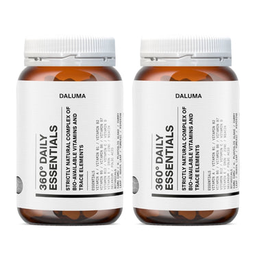 Zwei Flaschen Daluma 360 DAILY ESSENTIALS SUPPLEMENT DOUBLE mit weißen Etiketten und orangefarbenen Verschlüssen, nebeneinander auf weißem Hintergrund. Der Text auf dem Etikett ist verschwommen und unleserlich.