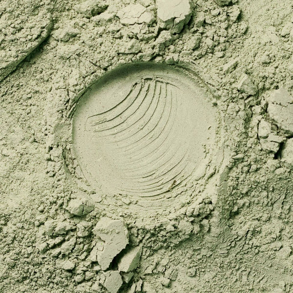 Nahaufnahme von hellgrünem Pulver mit einem kreisförmigen Abdruck in der Mitte, der durch mehrere gebogene, parallele Rillen gekennzeichnet ist. Zerbröckelte Pulverstücke umgeben den Abdruck.