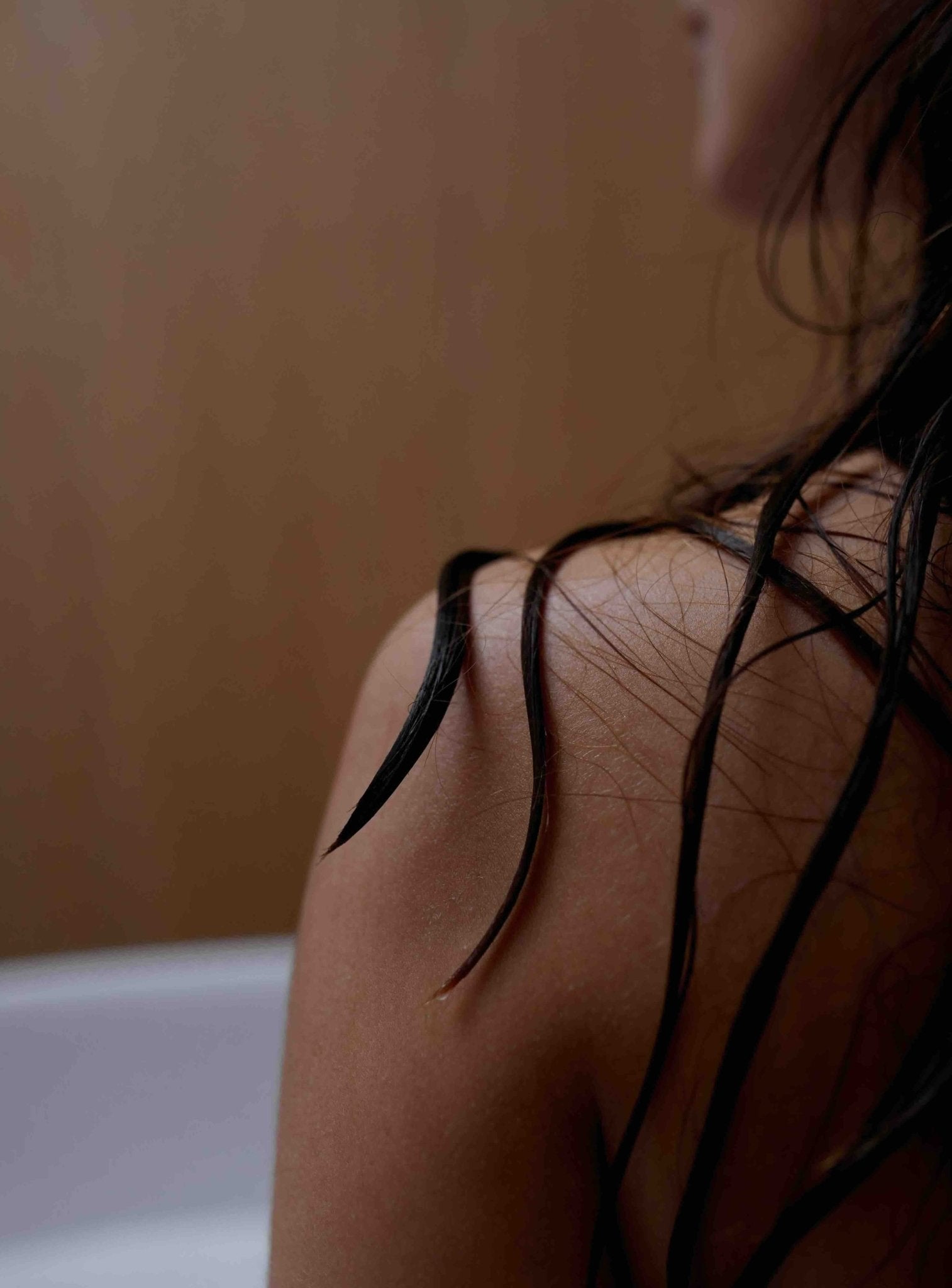 Eine Nahaufnahme einer nassen Schulter und dunklen Haaren mit Wassertropfen, die das gesunde Wachstum nach der Anwendung des Daluma-shop HAIR CARE DUO for vegane Haarpflege hervorheben. Der unscharfe Hintergrund unterstreicht die lebendigen Strähnen; das Gesicht ist teilweise sichtbar.