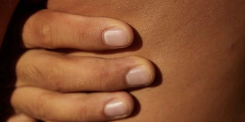 Eine Nahaufnahme einer Hand mit kurzen, sauberen Fingernägeln, die sanft auf der nackten Haut ruhen, wobei die Textur und die natürliche Farbe der Hand und der Haut hervorgehoben werden.