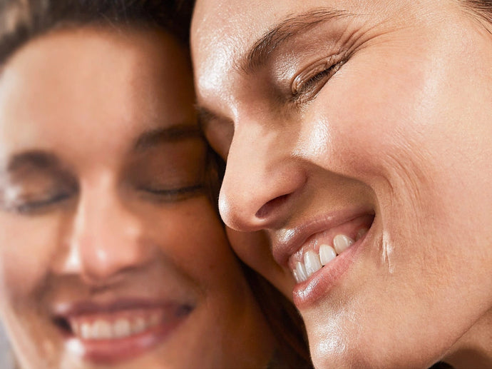 Eine Nahaufnahme einer lächelnden Person mit reiner Haut, deren Gesicht sich in einem Spiegel spiegelt, beide Bilder zeigen Glück und einen glatten, gesunden Teint.