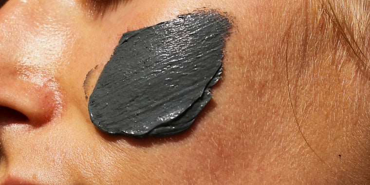 Eine Nahaufnahme einer Person mit einer dicken Schicht dunkelgrauer Gesichtsmaske, die auf die Haut in der Nähe von Augen und Nase aufgetragen wurde.