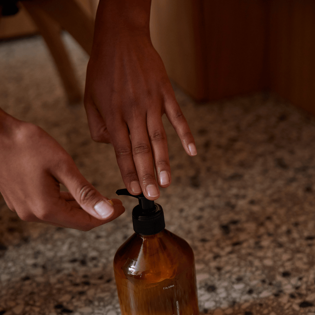 Die Hände drücken auf die Pumpe eines DALUMA FOREST SEED GEL HAND WASH-Spenders, der aus natürlichen Inhaltsstoffen hergestellt wird, und die Flasche steht auf einer gesprenkelten Arbeitsplatte.
