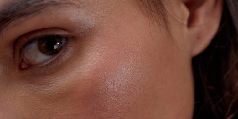 Nahaufnahme des Gesichts einer Person, mit Schwerpunkt auf dem linken Auge, dem Wangenknochen und einem Teil des Ohrs. Die Haut erscheint glatt mit einem natürlichen Schimmer und dezenter Röte. Das Haar der Person ist rechts teilweise sichtbar.