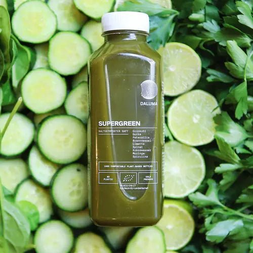 Eine Flasche DALUMA GRÜNE SAFTKUR - 3 TAGE steht auf geschnittenen Gurken, Limetten und Blattgemüse. Sein klares Design mit weißem Deckel und Text hebt die frischen Zutaten hervor und macht ihn ideal für jede Saftkur.