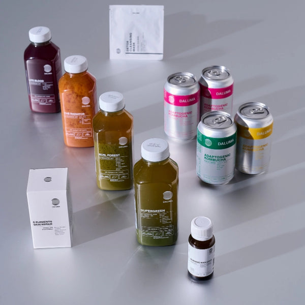 Eine Vielzahl von abgefüllten Säften, Dosen, kleinen Flaschen und Schachteln mit bunten Etiketten sind auf einer hellgrauen Fläche angeordnet und präsentieren eine Auswahl an Wellness-Getränken und Nahrungsergänzungsmitteln.