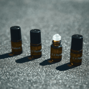 Vier kleine Braunglasflaschen aus dem Nullpunkt NULLPUNKT DISCOVERY SET stehen in einer Reihe auf einer strukturierten Oberfläche. Jede ist mit weißer Schrift versehen, drei haben schwarze Kappen, die zweite von rechts hat einen weißen Rollerball-Verschluss.