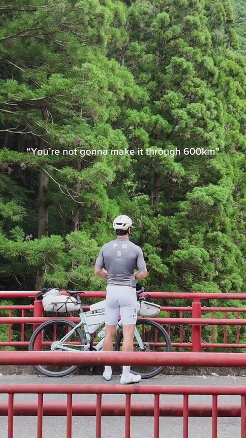 Ein Radfahrer in grauer Kleidung steht mit einem beladenen Fahrrad auf einer roten Brücke, vor dichten grünen Bäumen. Der Text darüber lautet: "Du wirst es nicht schaffen, 600 km zu fahren".