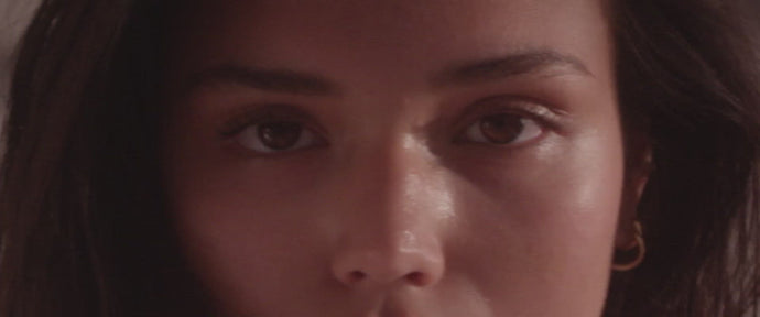 Nahaufnahme des Gesichts einer Person, wobei der Schwerpunkt auf den Augen und den oberen Wangen liegt, mit glatter Haut, dunklem Haar und einem goldenen Reifohrring auf der rechten Seite.