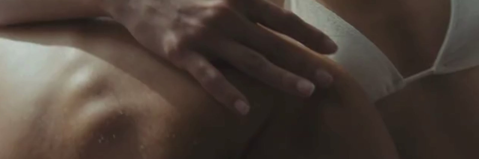 Eine Nahaufnahme einer Person, die einen weißen BH trägt und mit ihrer Hand den nackten Rücken einer anderen Person berührt, was einen intimen oder tröstenden Moment andeutet.