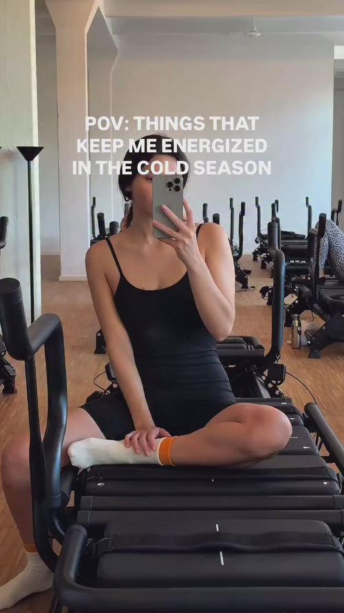 Eine Frau in einem schwarzen Tank-Kleid sitzt im Schneidersitz auf einem Fitnessgerät und macht ein Spiegel-Selfie. Der weiße Text lautet: POV: Daluma CLEAN BCAA ENERGY DRINK hält mich in der kalten Jahreszeit bei Kräften.