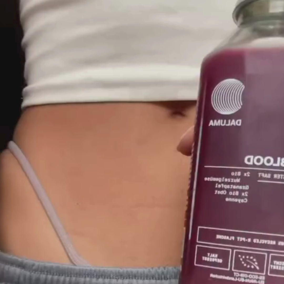 Nahaufnahme des Unterleibs einer Person in einem hellvioletten Hosenbund, die eine mit violetter Flüssigkeit gefüllte Flasche Daluma BETTER SHAPE SAFTKUR 3 TAGE Saft hält.