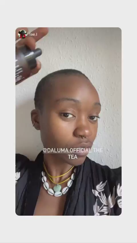 Eine Person mit kurzem Haar trägt ein Produkt auf ihre Kopfhaut auf. Sie trägt eine Muschelhalskette, einen Nasenring und ein schwarz gemustertes Oberteil. Der Text @DALUMA.OFFICIAL THE TEA erscheint über dem Bild.