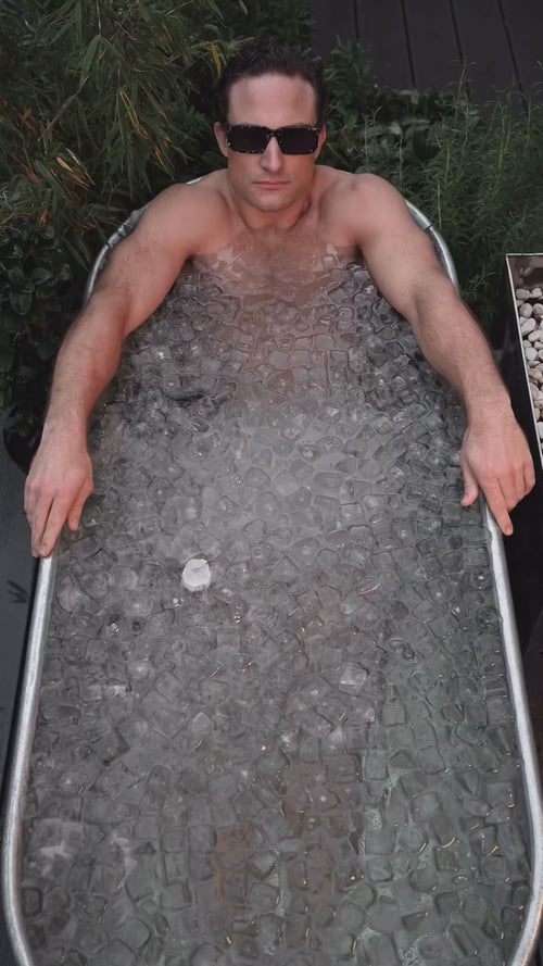 Eine Hand hält zwei grüne Daluma-Saftflaschen aus dem "GRÜNE SAFTKUR - 5 TAGE"-Programm mit weißen Verschlüssen und Etiketten mit weißer Schrift und Grafik über verstreuten Eiswürfeln.