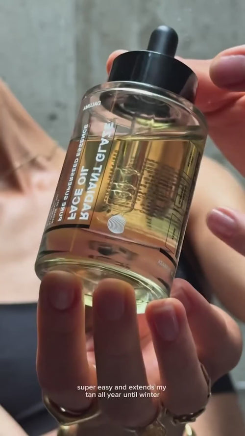 Eine Hand hält eine klare Tropfflasche mit der Aufschrift Daluma RADIANT GLAZE GESICHTSÖL, die mit einer goldenen Flüssigkeit gefüllt ist. Der unscharfe Hintergrund hebt den Text hervor: Super einfach und hält mein Strahlen das ganze Jahr über, sogar im Winter.