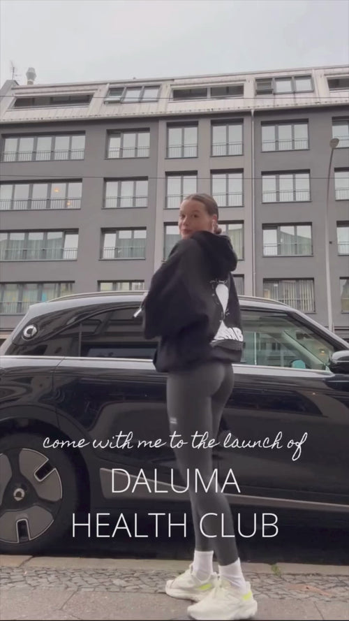 Eine sportlich gekleidete Person steht vor einem schwarzen Auto und einem modernen Gebäude. Der Text lautet: Begleiten Sie mich bei der Einführung der HEALTH CLUB PRO MEMBERSHIP von Daluma.