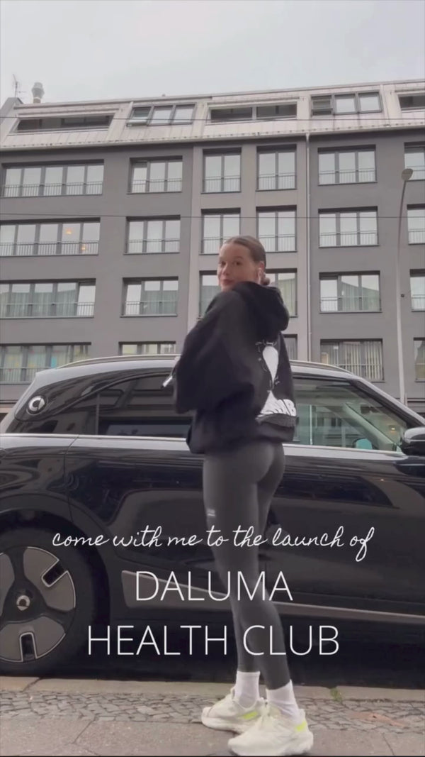 Eine sportlich gekleidete Person steht vor einem schwarzen Auto und einem modernen Gebäude. Der Text lautet: Begleiten Sie mich bei der Einführung der HEALTH CLUB PRO MEMBERSHIP von Daluma.