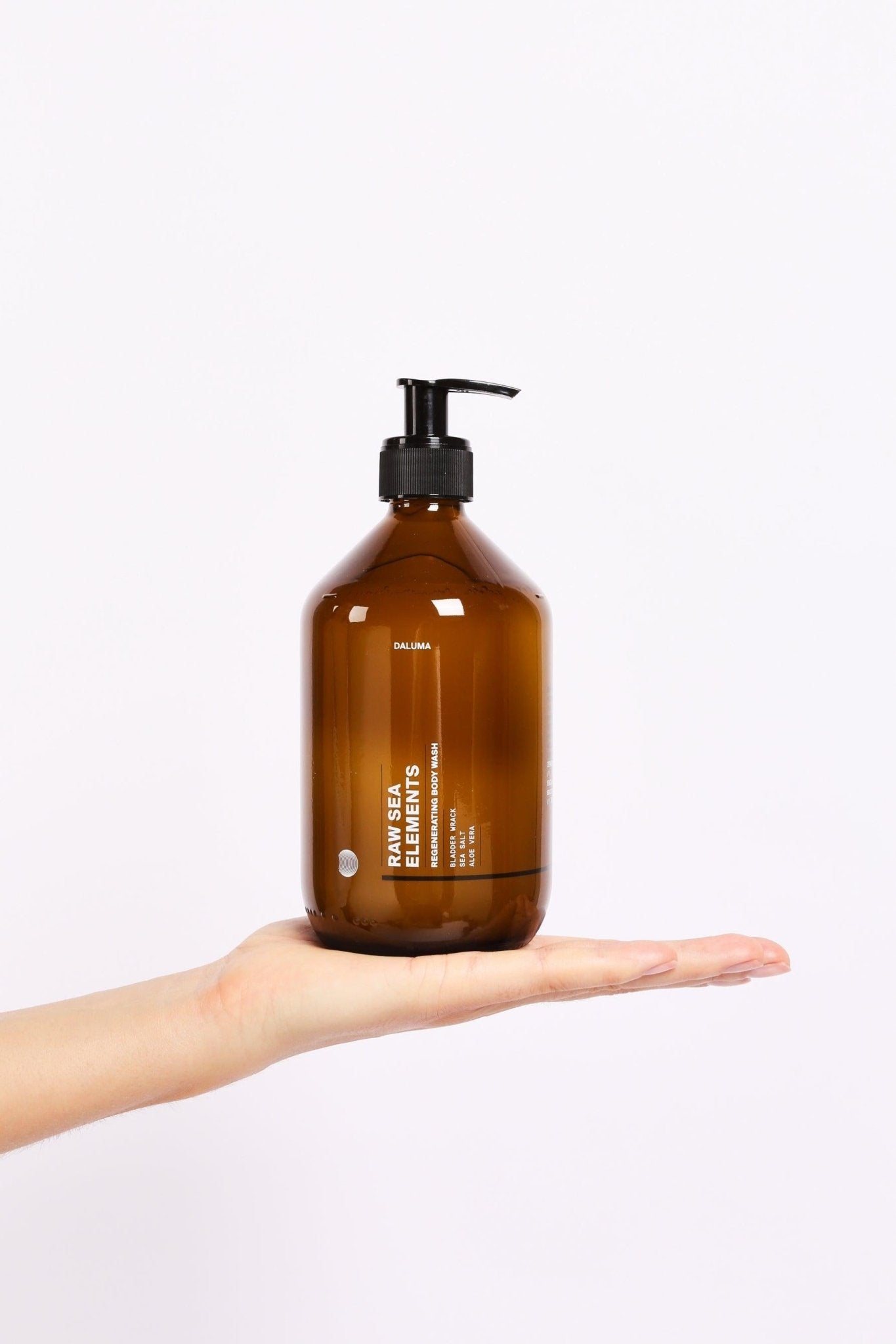 Eine braune Pumpflasche aus dem BODY CARE DUO von Daluma-shop wird auf einer ausgestreckten Hand vor einem schlichten weißen Hintergrund balanciert.