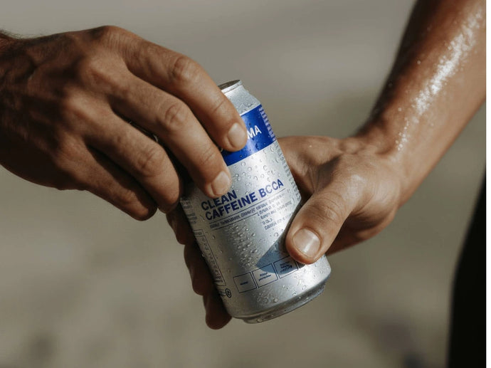 Nahaufnahme von zwei Händen, die eine kalte, silberne Dose mit der Aufschrift Clean Caffeine BCAA halten, auf deren Oberfläche sich Kondenswasser bildet, was darauf hindeutet, dass sie frisch gekühlt ist.